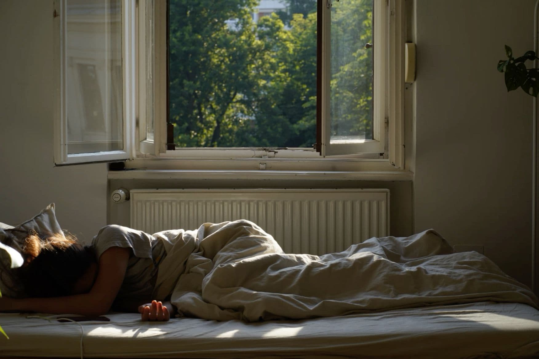 A person sleeping beneath rumpled bedding in a softly sunlit bedroom